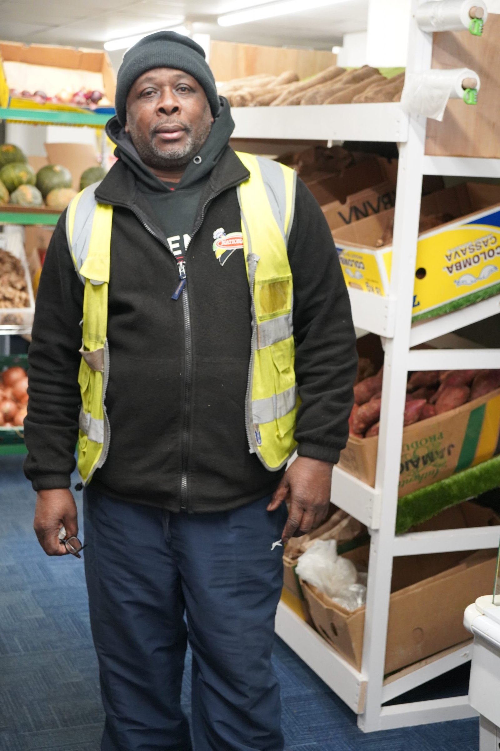 A picture showing the store owner stand next to some produce